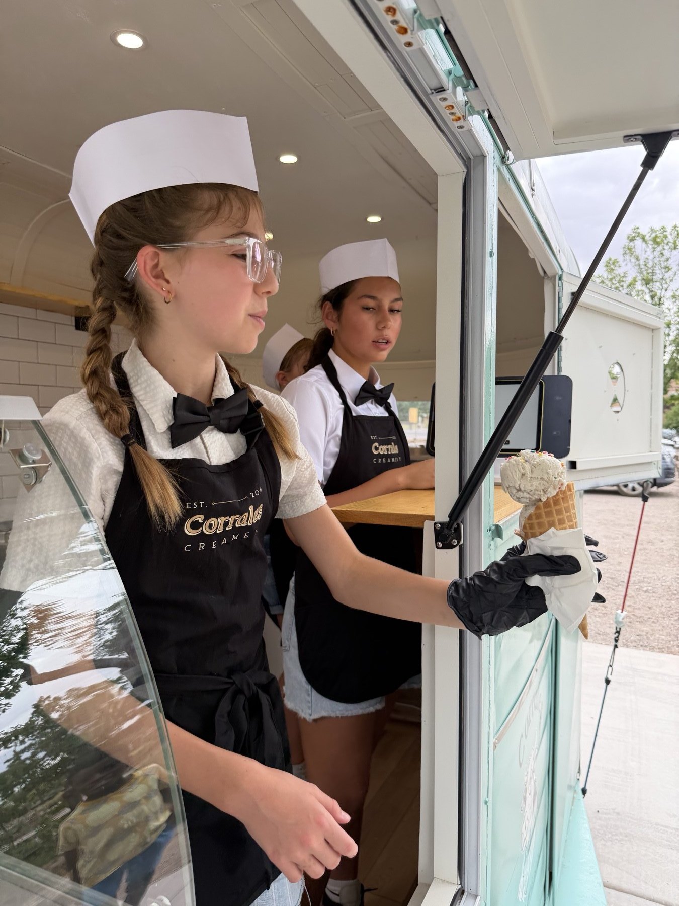 Two servers preparing a fresh waffle cone in the trailer