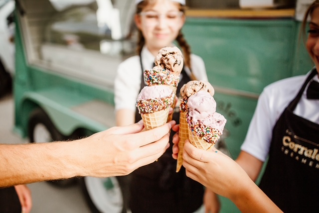 Four waffle cones of hand-scooped ice cream raised in a toast beside the trailer