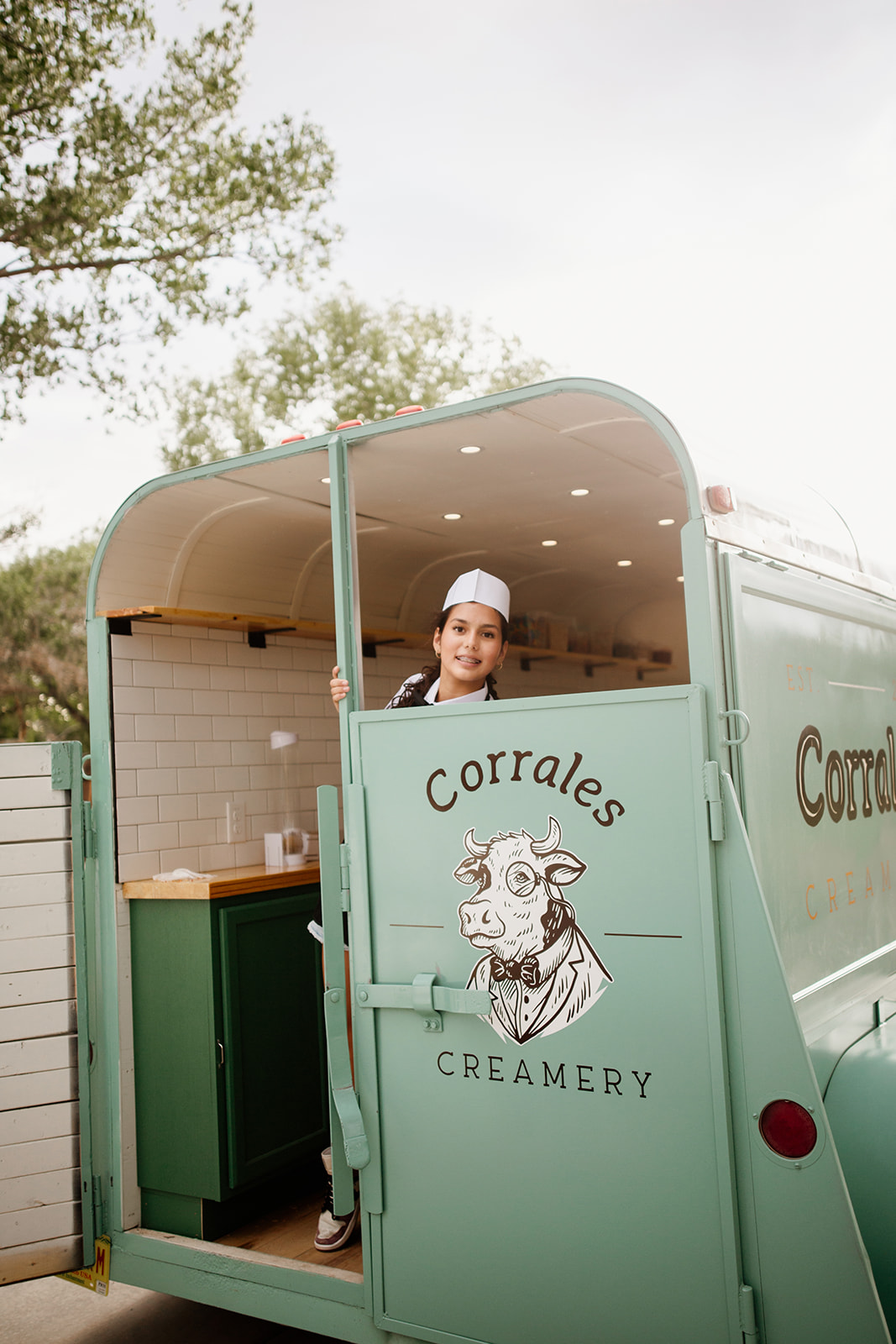 A smiling server in the doorway of the mint-green Corrales Creamery trailer